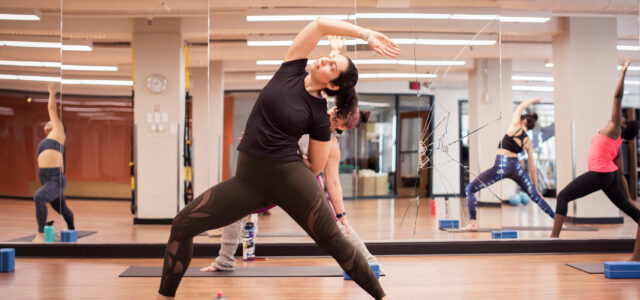 Female athletes practicing extended side angle pose on exercise mats against mirror in gym