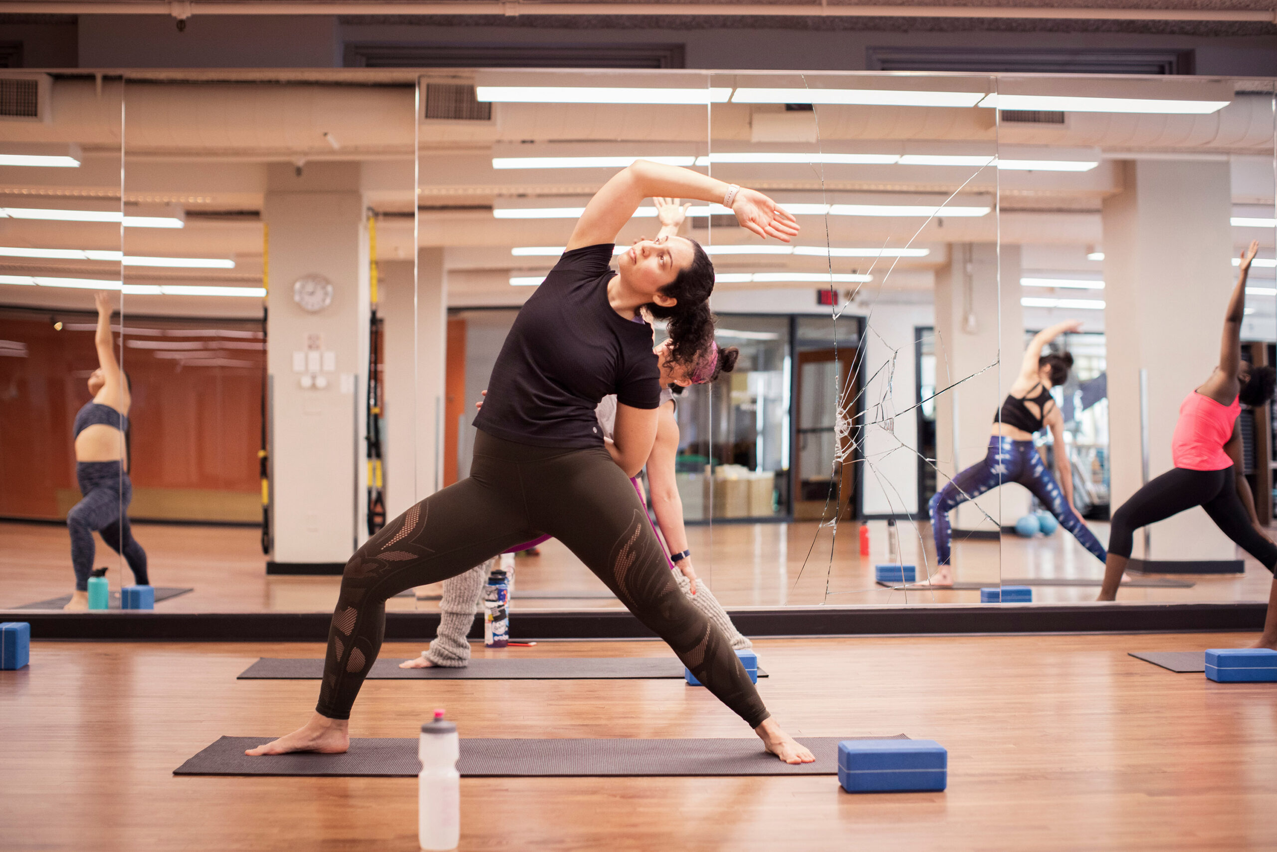 Female athletes practicing extended side angle pose on exercise mats against mirror in gym